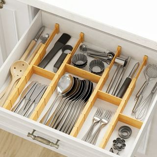 An open white kitchen drawer filled with silver cutlery, divided up into categories by bamboo drawer divders