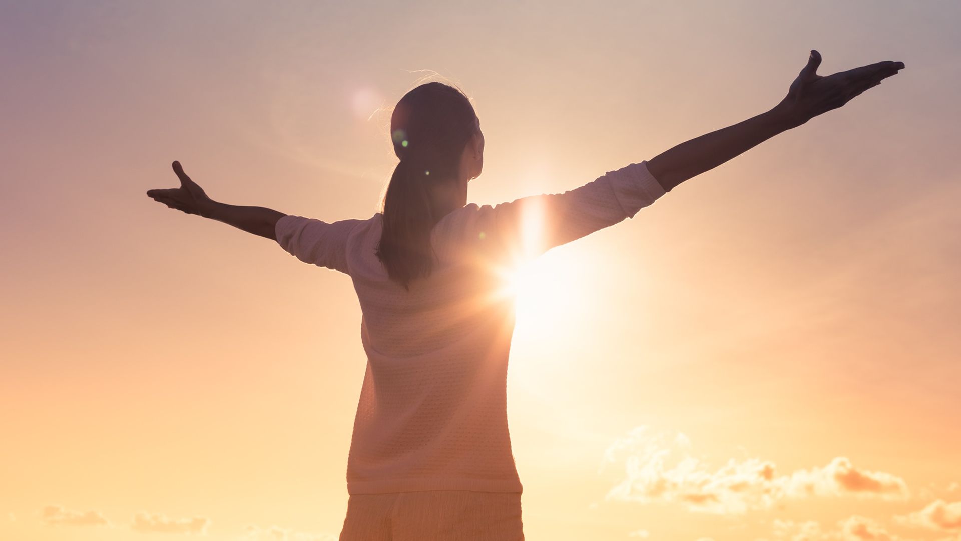 A woman faces a sunset and spreads her arms in a relaxed manner.