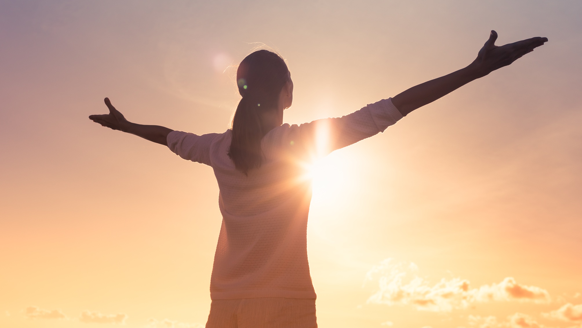 A woman faces a sunset and spreads her arms in a relaxed manner.