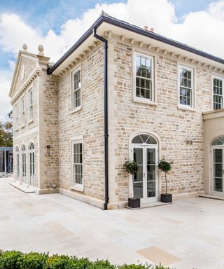 Large Geogian-style detached property clad in light buff stone, with sash windows and black Yeoman Rainguard rainwater goods