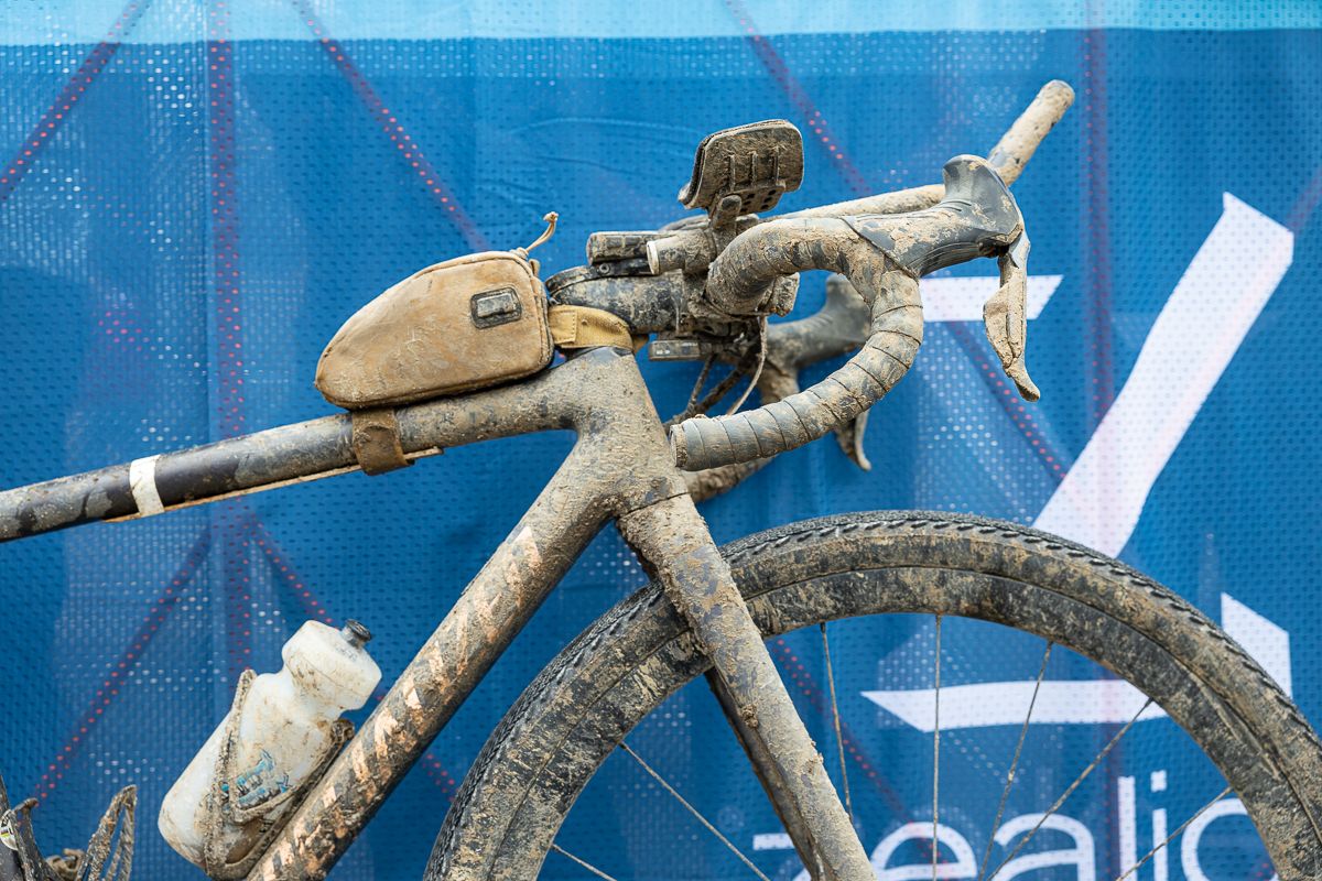 The front of a gravel race bike with a feed bag covered in slop
