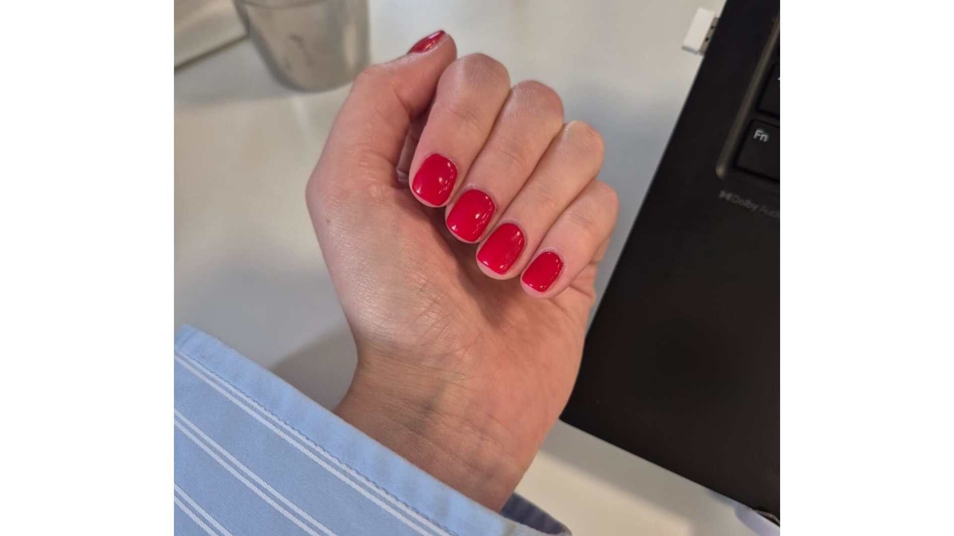 Image of Naomi Jamieson's cherry red short square nails and wearing a blue striped shirt