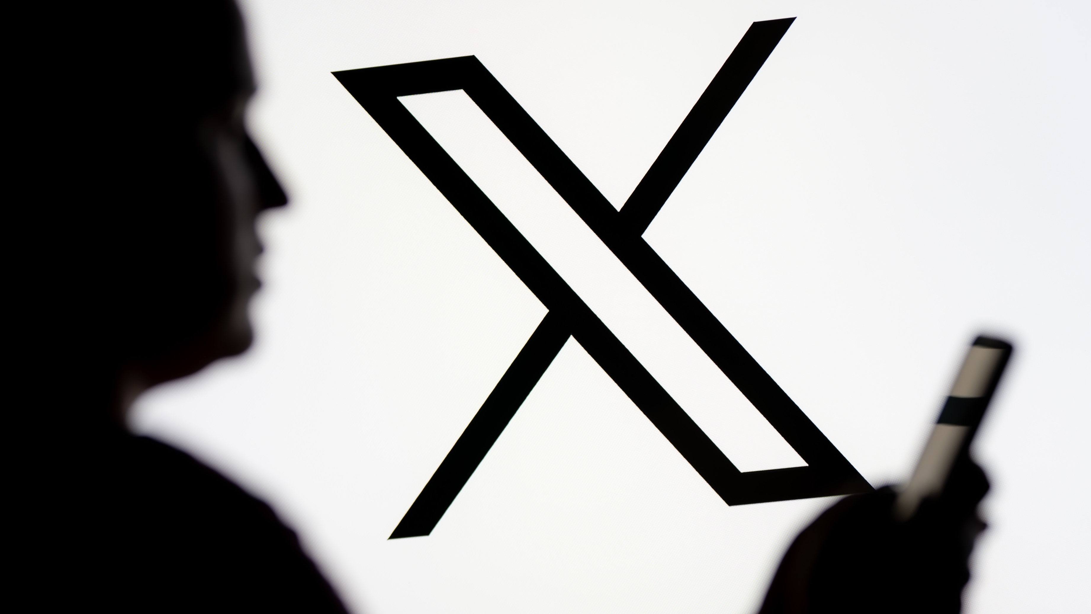 The silhouette of a person looking at a phone screen in front of the logo for the social media platform X
