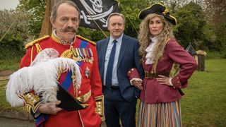 Kevin Whately in a red jacket and holding a feathered hat alongside Neil Dudgeon in a suit and Fiona Dolman in a red jacket and black hat in Midsomer Murders 