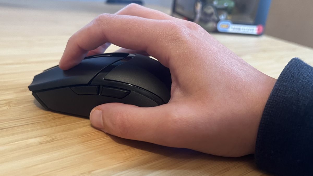 Reviewer's hand using Razer Cobra Hyperspeed in a claw grip on a wooden desk