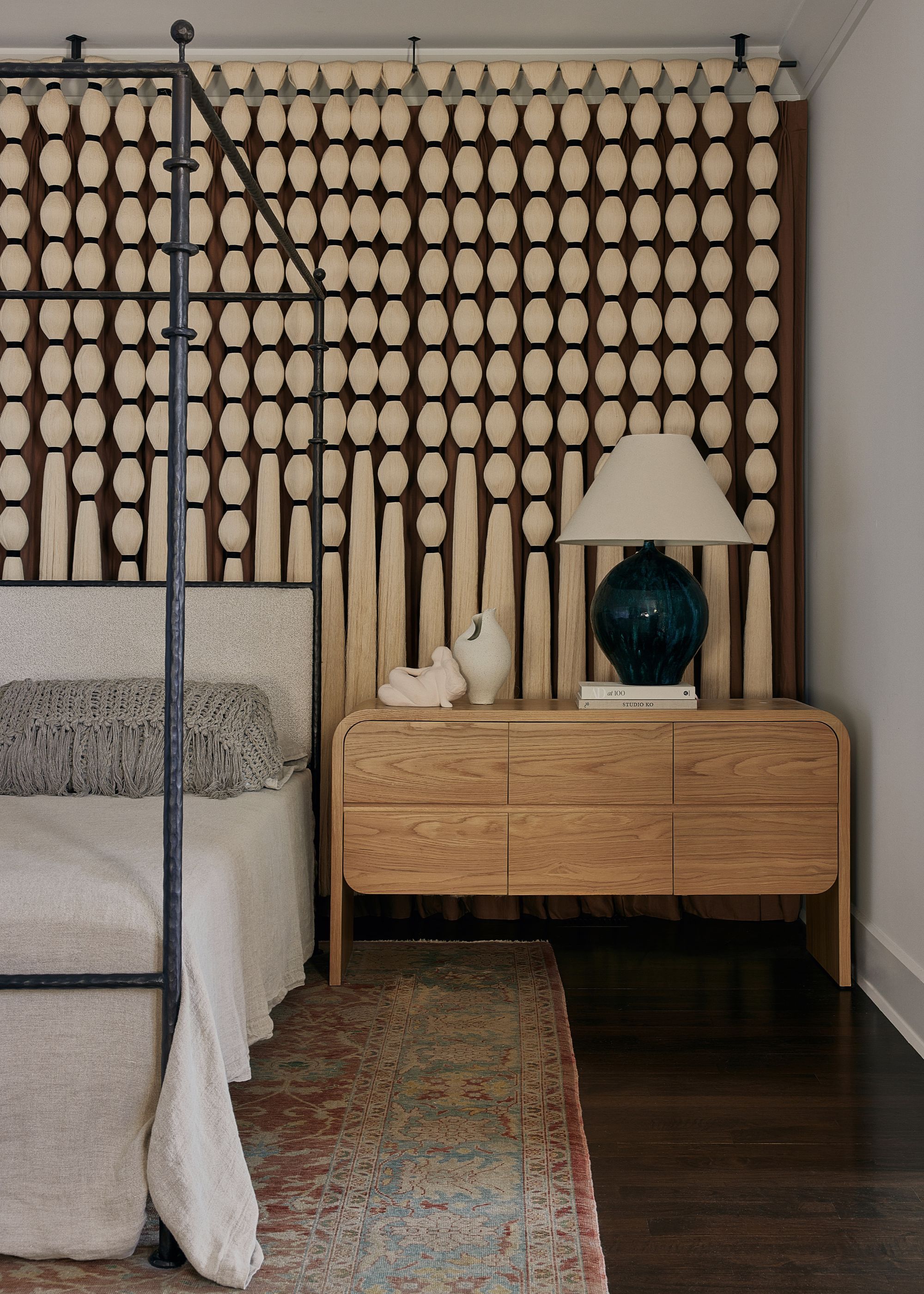 A corner in the master bedroom with a four-poster bed, vintage carpet, tassels used as curtain and two wooden side tables 