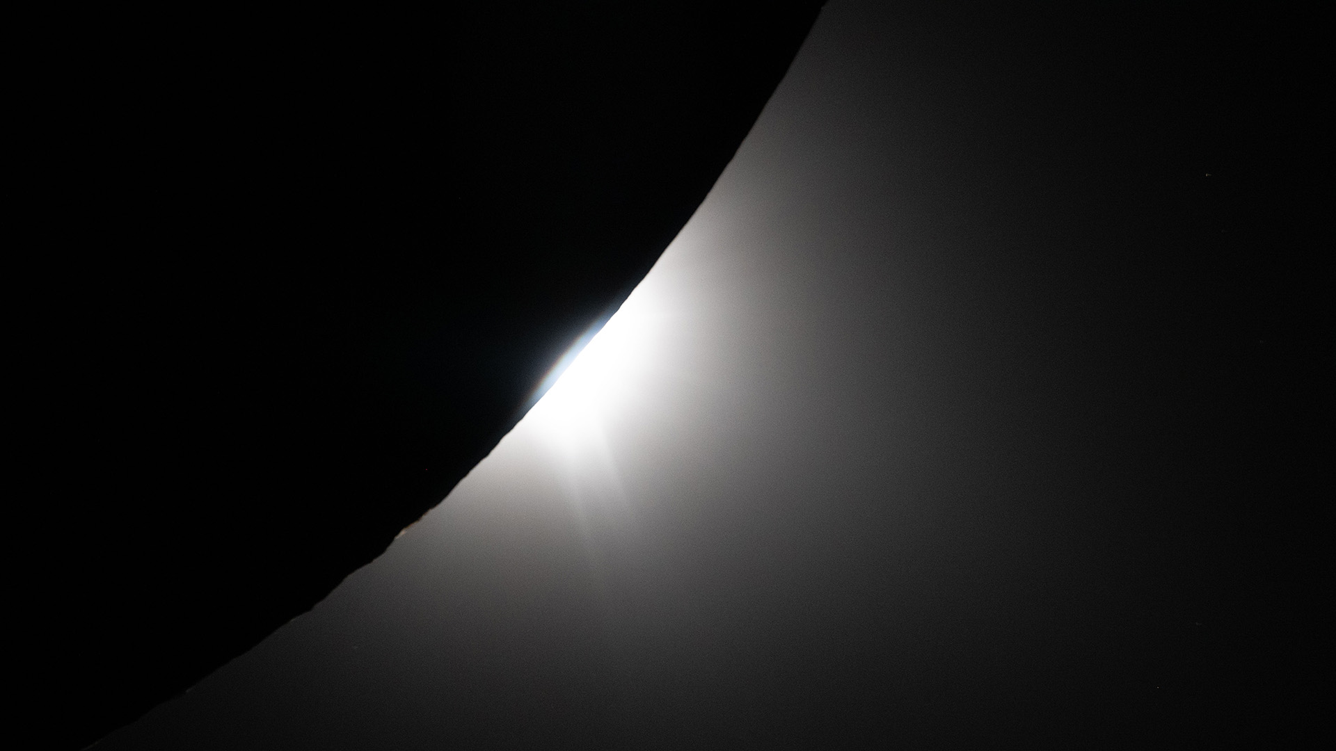 A silhouette of the curve of the bottom half of the moon, with glowing white light behind it.