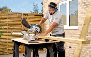 male cutting wood in garden area using saw