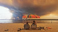 TOPSHOT - Beach goers rest on the beach of Moutchic on the shore of Lake Lacanau (Etang de Lacanau) in Lacanau , southwestern France on July 24, 2026, as clouds of smoke rise into the sky from the Gironde wildfire. The fire raging in the northern part of the Arcachon Basin in Gironde, southwest France, has swept through more than 3,400 hectares, according to the latest figures released by the prefecture. More than 20,000 residents and tourists have been evacuated from this part already devastated by flames in 2022. Scientists have long warned that climate change caused by human use of fossil fuels will make periods of drought more intense and longer-lasting, creating the ideal conditions for wildfires. (Photo by Maximilien LAMY / AFP via Getty Images)