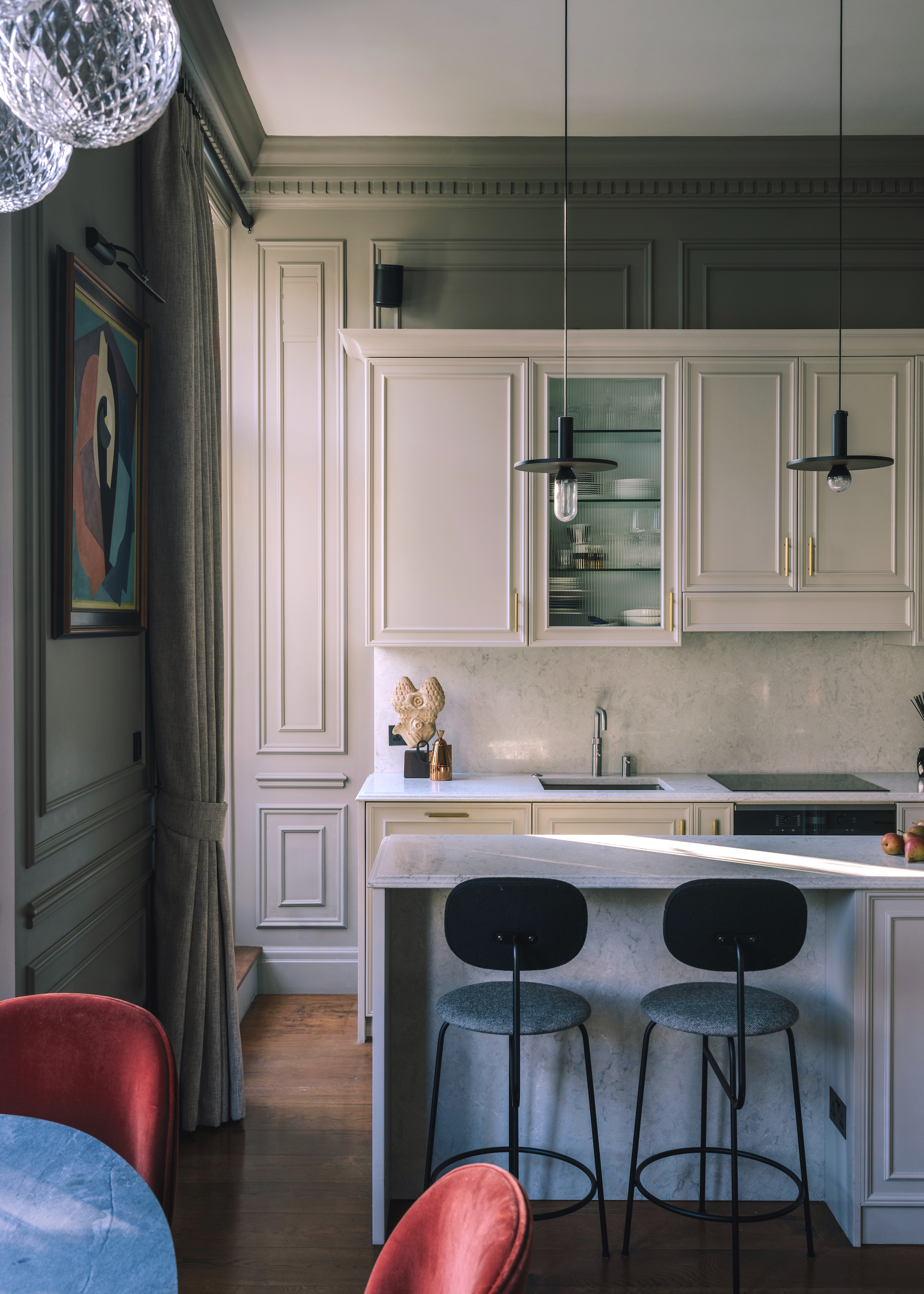 kitchen in off-white with green walls as well as a off white kitchen island in the middle with bar stools beside it