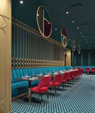 Liòn restaurant with teal banquette seating, red chairs and circles of brass as wall screens and ceiling medallions