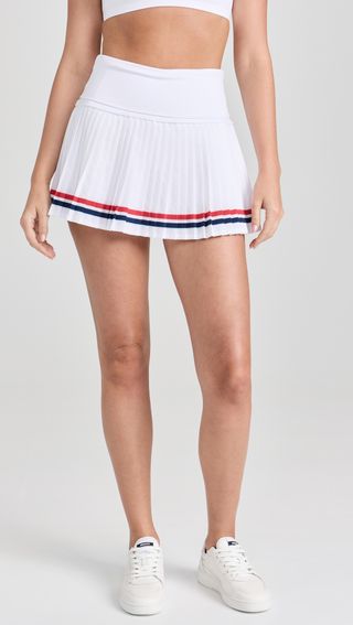 a model wears a white pleated tennis skirt with red and navy blue stripes 