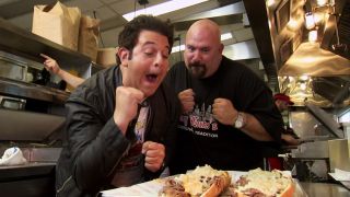 Adam Richman puts up his fists with another chef as they look at some philly cheesesteaks