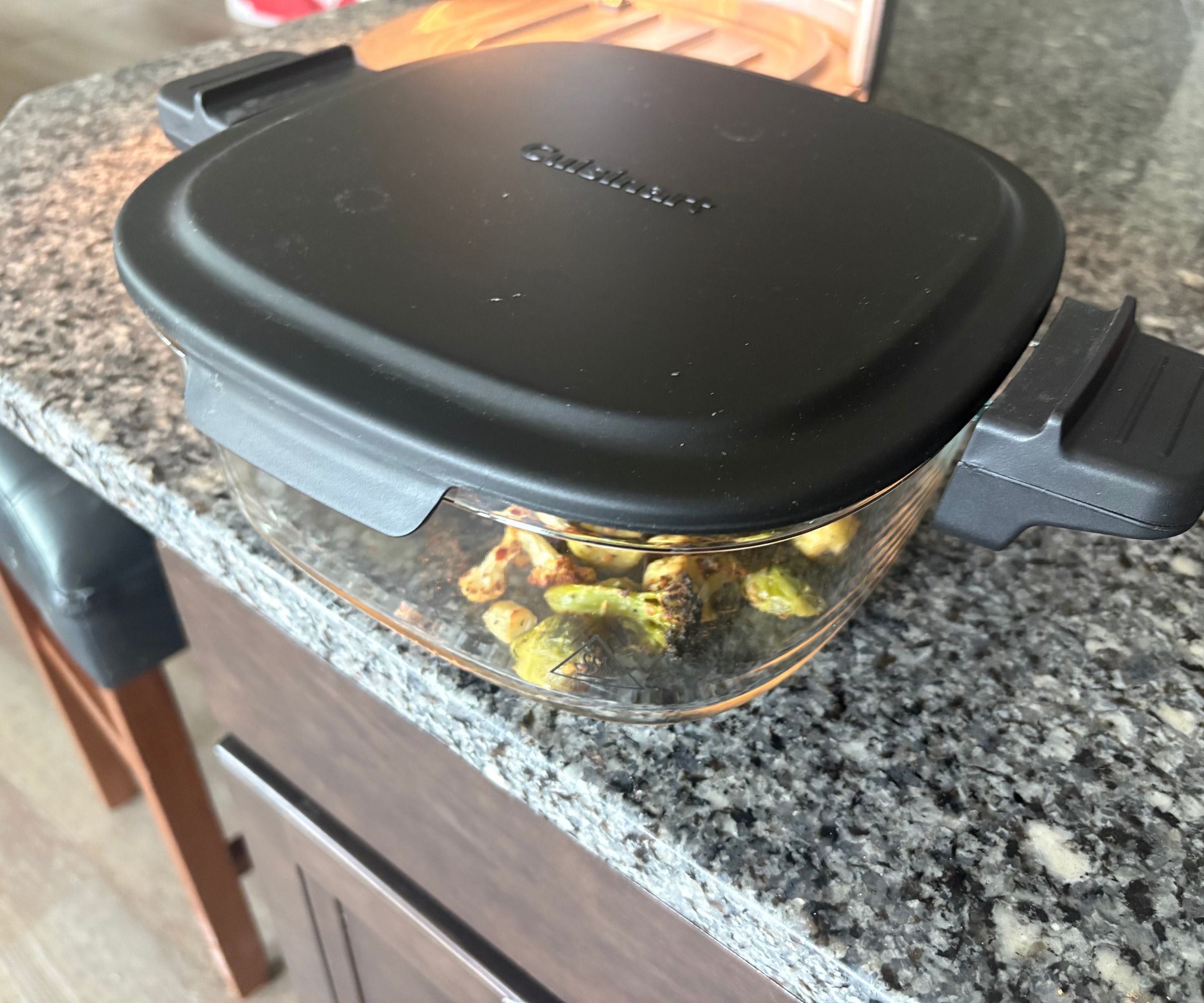 The glass basket of the Cuisinart glass air fryer on a granite countertop with the black lid securely on top.