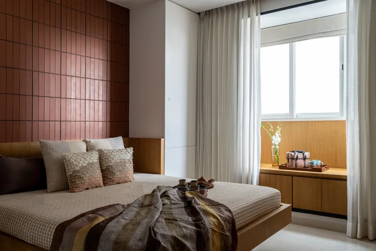 Bedroom with terracotta tiled wall behind bed, wooden window seat and neutral soft furnishings