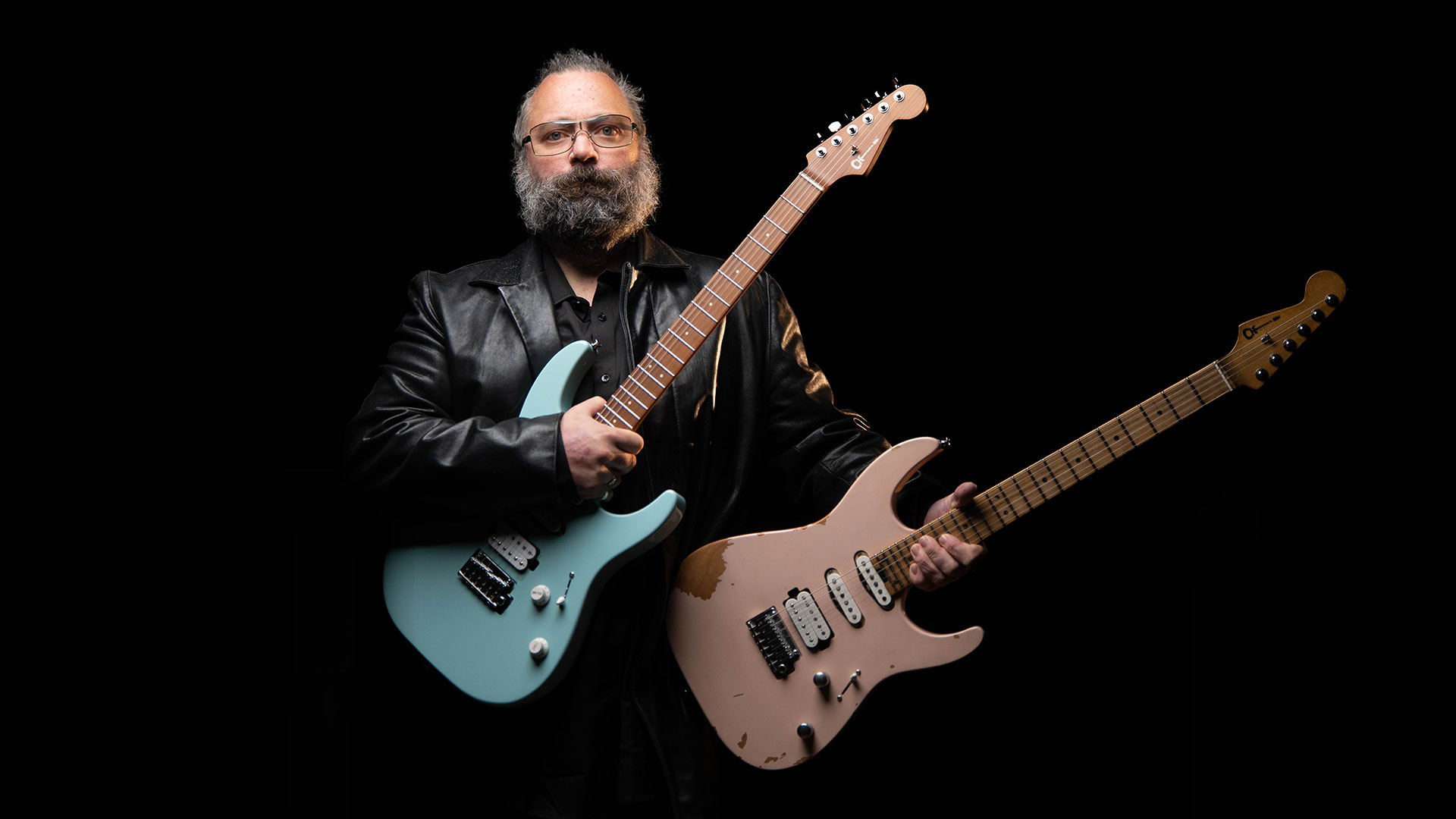 Rick Graham holds his two Charvel Signature guitars, against a black backdrop