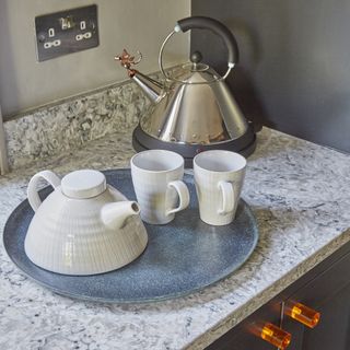 Grey fitted units with grey and white marbled worktop, copper handles, with tray of teapot, mugs and kettle