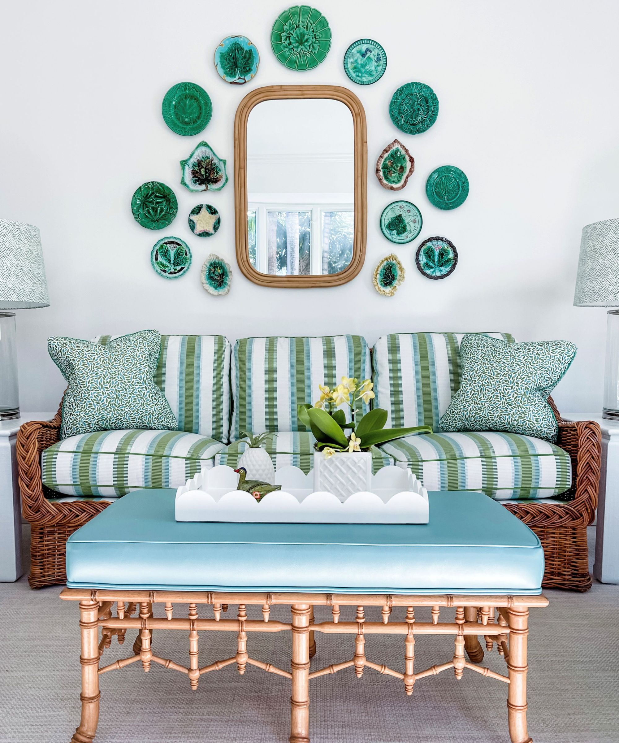 Coastal living room in blue and green with bamboo table, rattan sofa with striped cushions and majollica plate wall in green