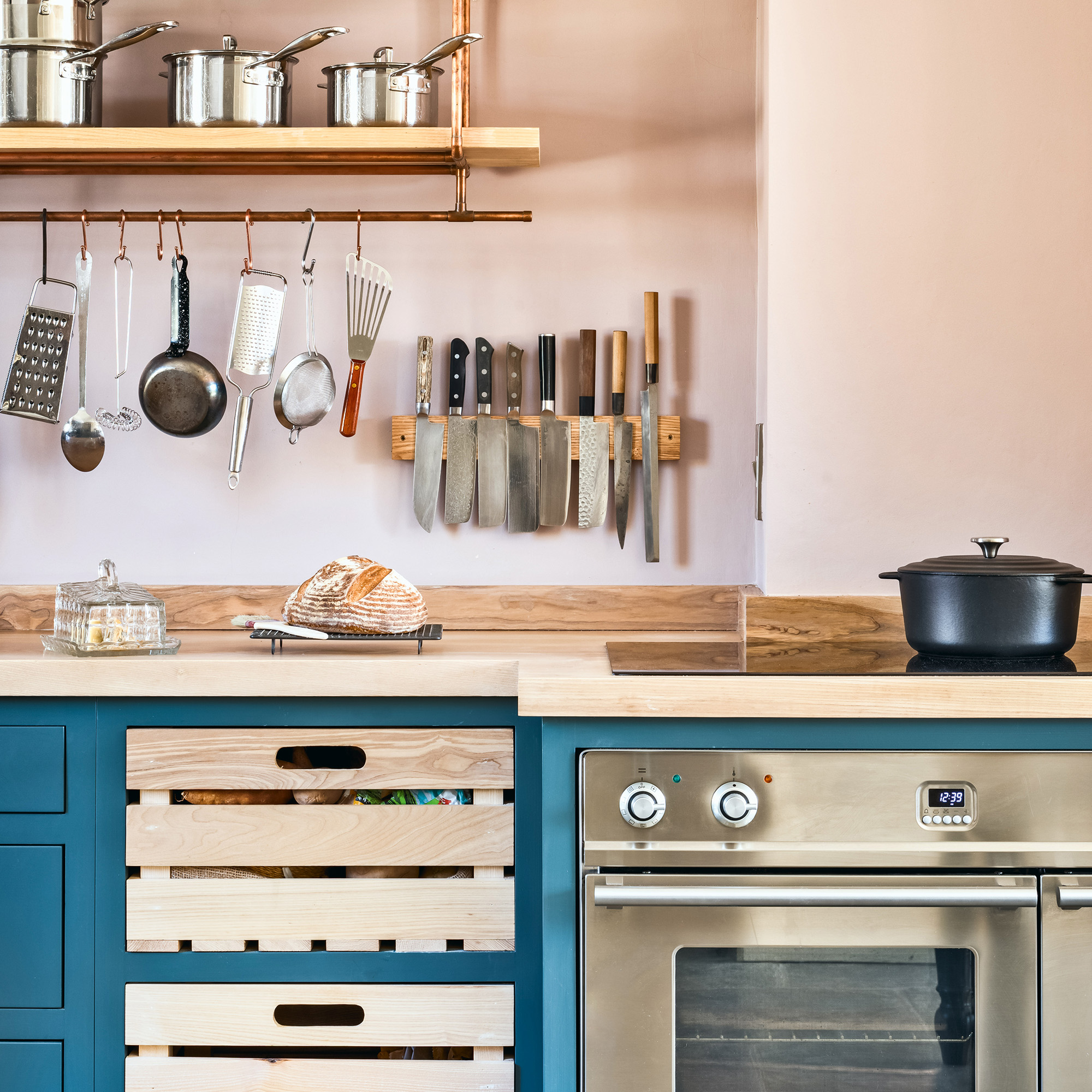 country kitchen with pink walls and blue cabinetry and with open shelf made from copper pipe and ash, knife block and open crate drawers