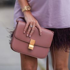 a hand wearing nude nail polish holding a bag