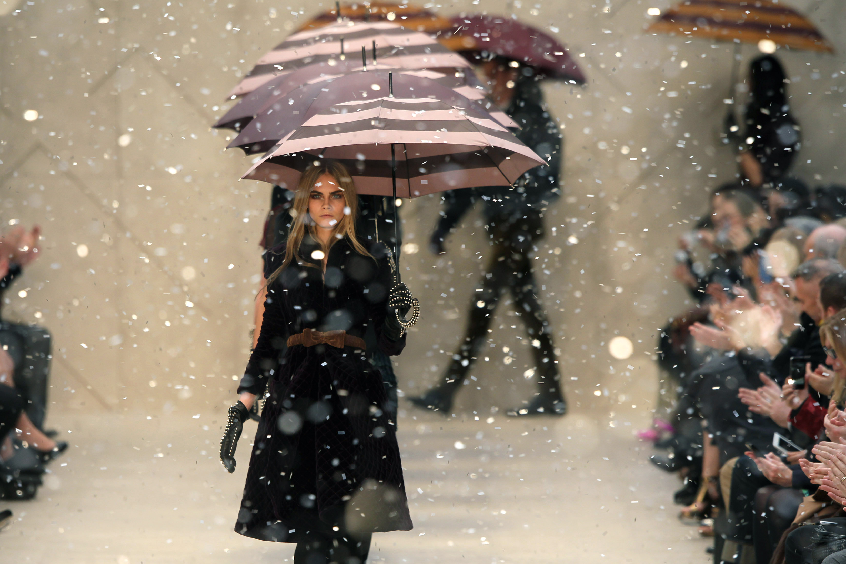Cara Delevigne walking down the Burberry catwalk holding an umbrella