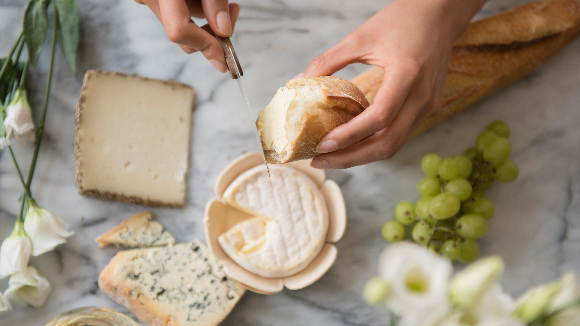 image shows a person cutting a baguette to dip into french cheese