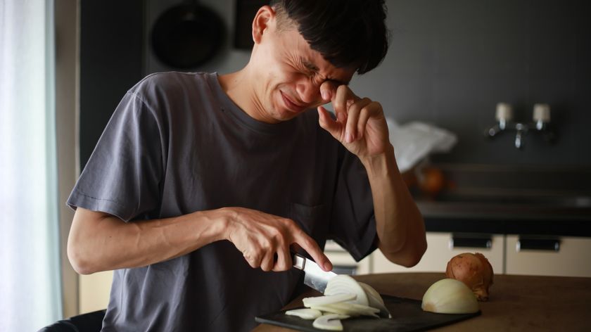 A man rubs his eye as he is cutting onions in his kitchen.