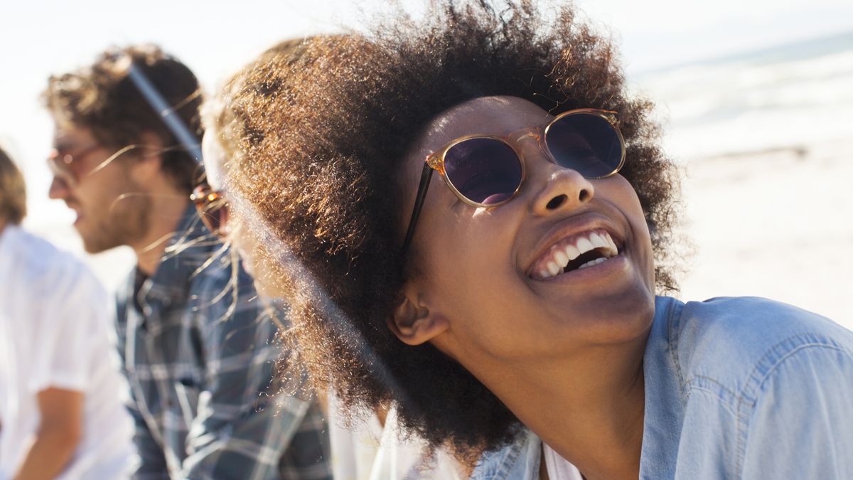 Eye health tips: A smiling woman wears sunglasses to protect her eyes in blazing sunshine