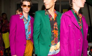 3 models line up wearing brightly coloured suits