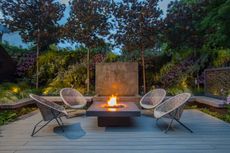 outdoor fireplace with four round wicker chairs facing a central firepit