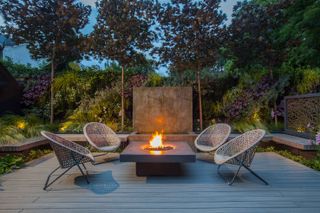 outdoor fireplace with four round wicker chairs facing a central firepit