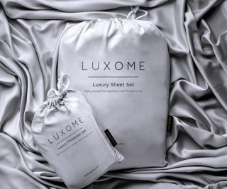 Luxome Luxury Sheet Set in a bag on top of bed sheets.