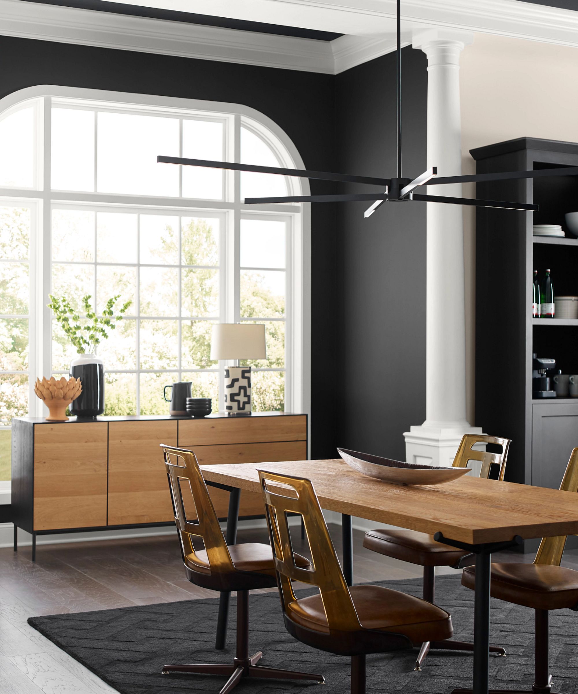 Dining room with black walls and white columns, wood midcentury dining table and chairs and black rug