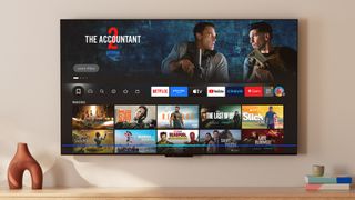 The Amazon Fire TV Omni QLED (2025 edition) displaying the Fire TV smart platform home screen in a living room setting