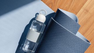 Yoga mat rolled up on ground on wooden floor, holding a water bottle