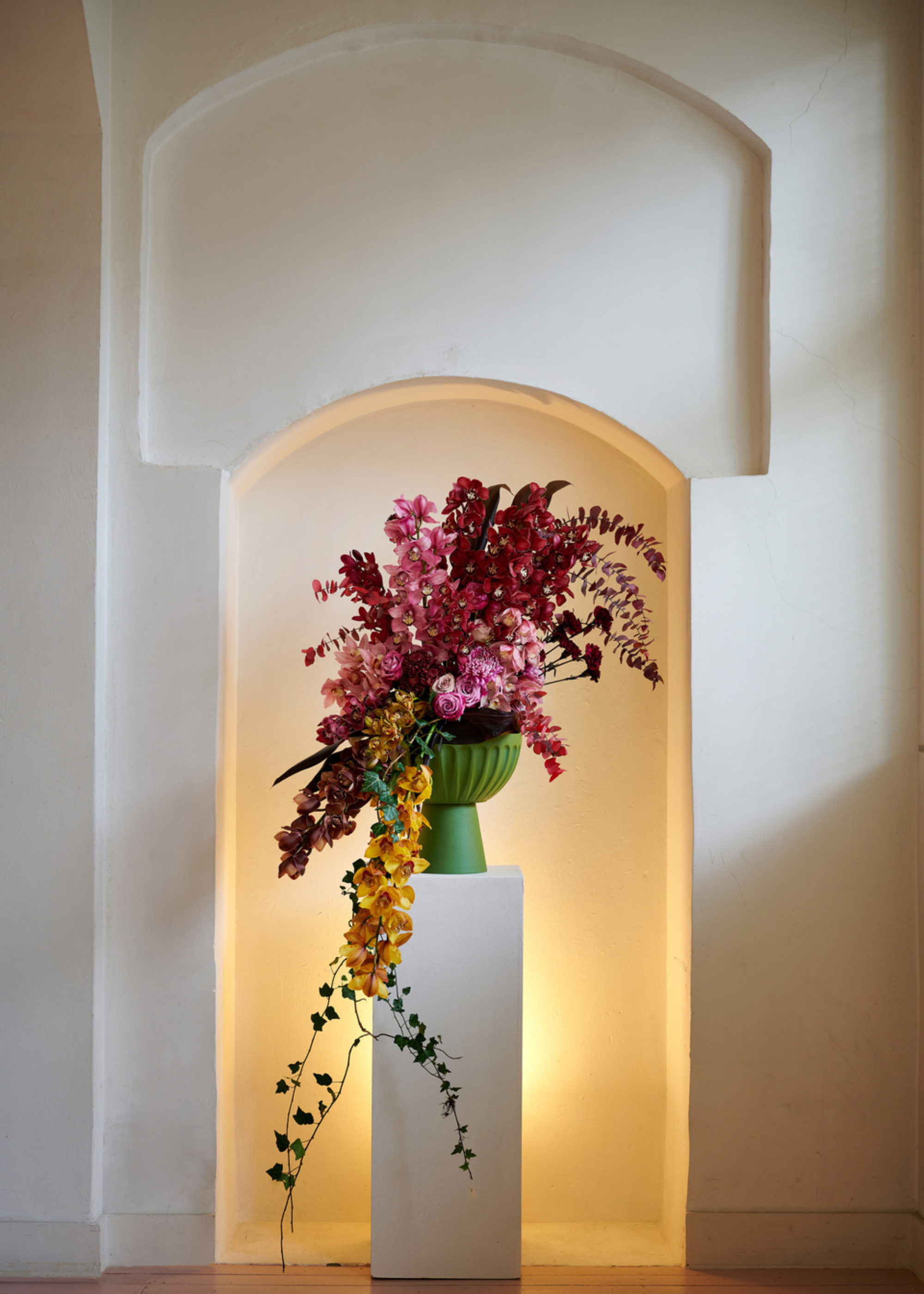 A pedestal vase with colorful flowers on a white pedestal with soft, yellow backlighting