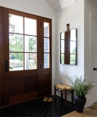 white small entryway with large mahogany doors with glass panels decorated with a mirror and small woven stool