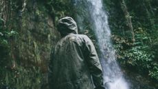best waterproof jacket: man standing in front of a waterfall wearing The North Face jacket