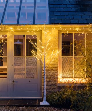 An example of outdoor lighting ideas showing a porch area with a lit fake tree and fairy lights above