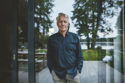 Senior man with hands in pockets standing in front of glass wall.