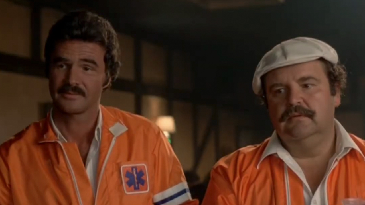 Burt Reynolds on the left and Dom DeLuise both in orange jackets in The Cannonball Run