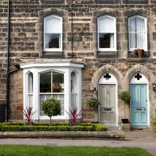 stone wall house with blue and cream coloured door white windows and plants