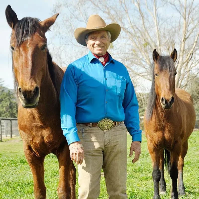 Monty Roberts posing with two horses