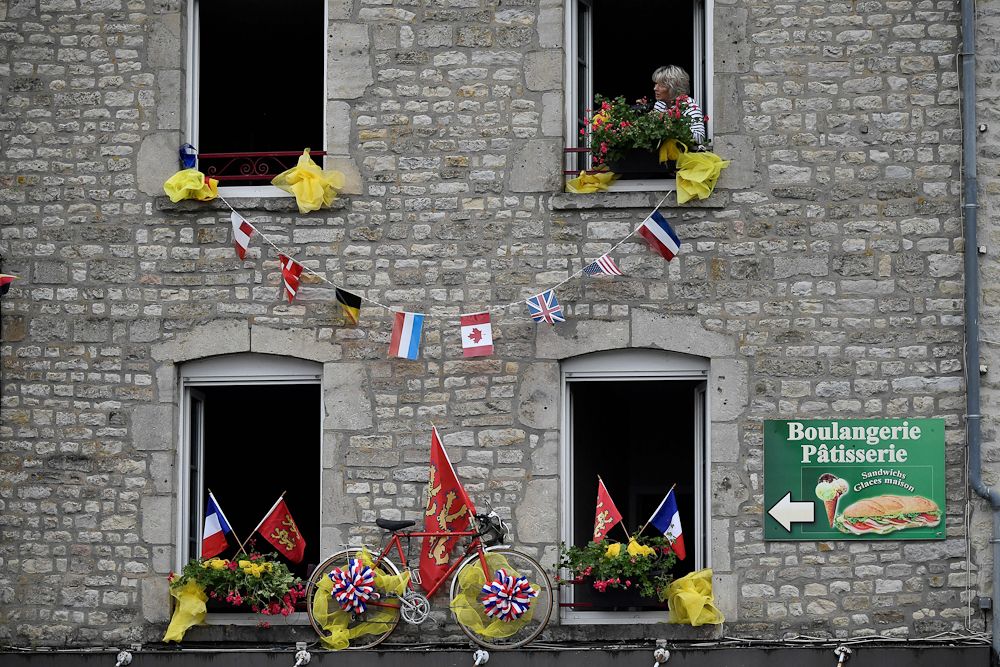 A bike is installed on the facade of an apartements building as a woman looks out from her window in Sainte-Marie-du-Mont, Normandy, on July 30, 2016, two days before the start of the 103rd edition of the Tour de France