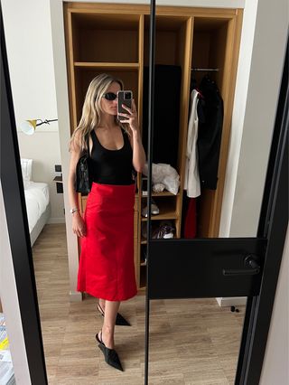 Eliza Huber wearing a black Agolde tank top with a red Ferragamo duchesse satin midi skirt and black Prada heels.