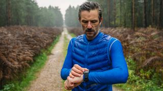 a male trail runner dressed in moisture wicking layers looking at his GPS watch