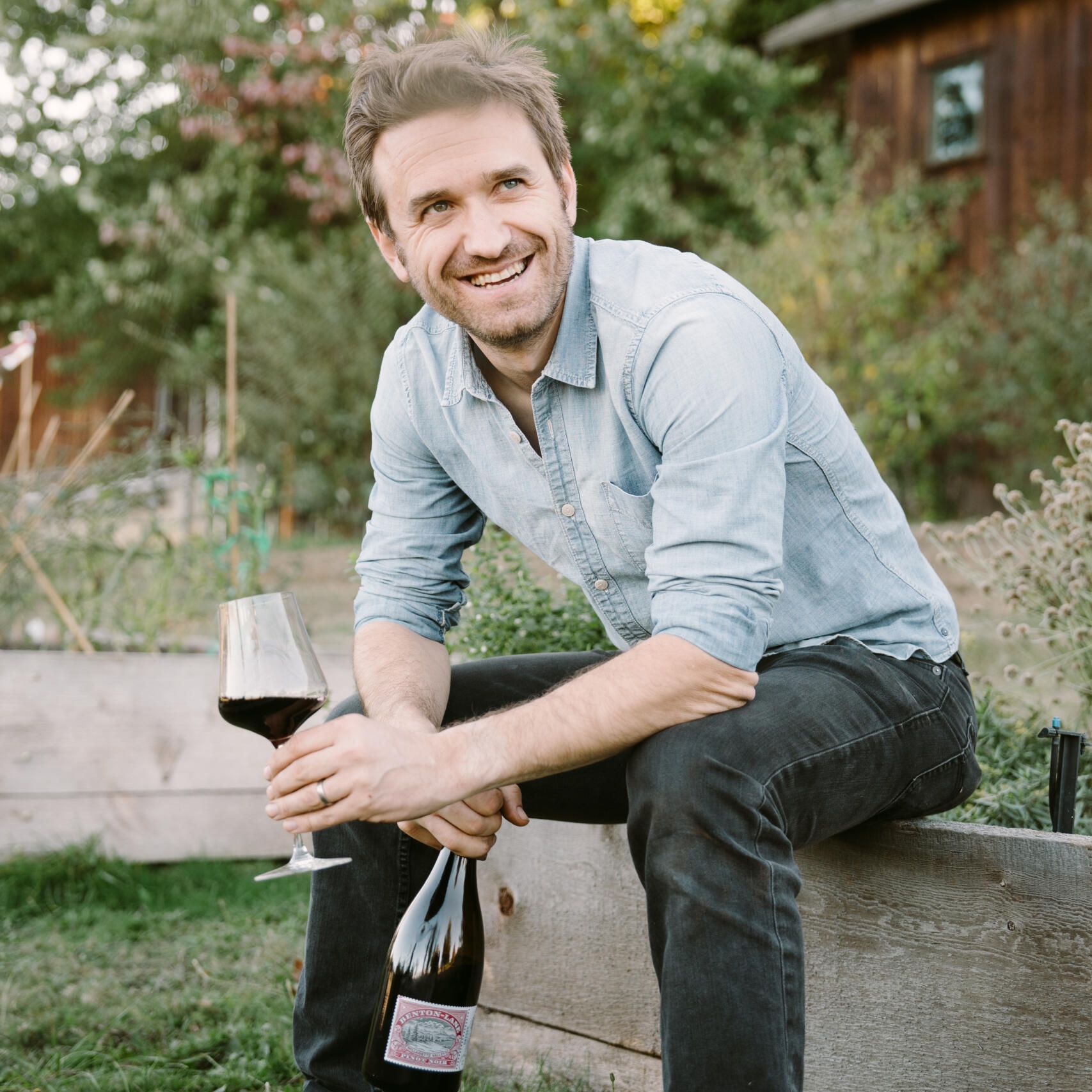 Portrait of winemaker Amael Orrego holding a bottle and glass of Benton Lane Pinot Noir