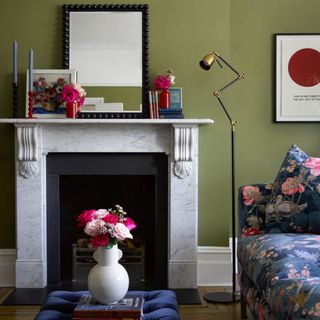 living room colour schemes, green living room with marble fireplace, floral sofa, blue footstool, flowers on footstool and mantel, candlesticks on mantel with black beaded mirror, vintage style floor lamp