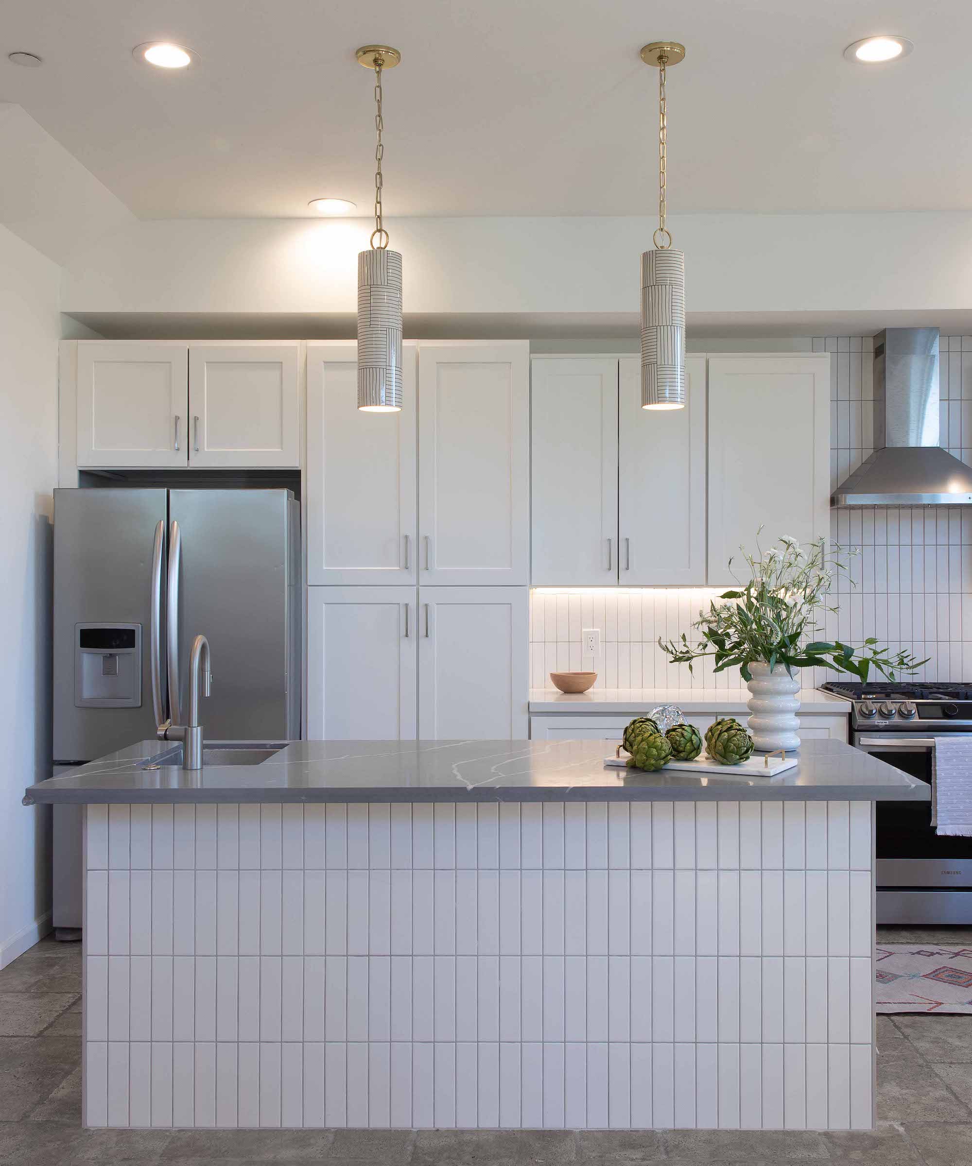 Kitchen with white cabinets and white island with tile front and pendant lights above