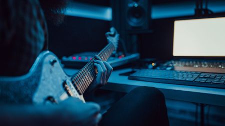 Young man playing electric guitar in the control room of a recording music studio